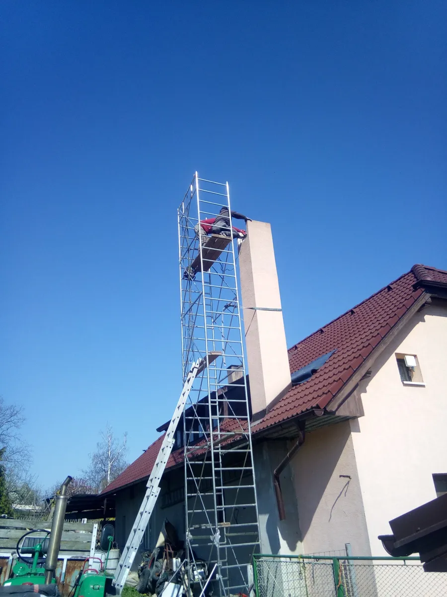 Pracovník na lešení montuje nerezový komín na střeše rodinného domu