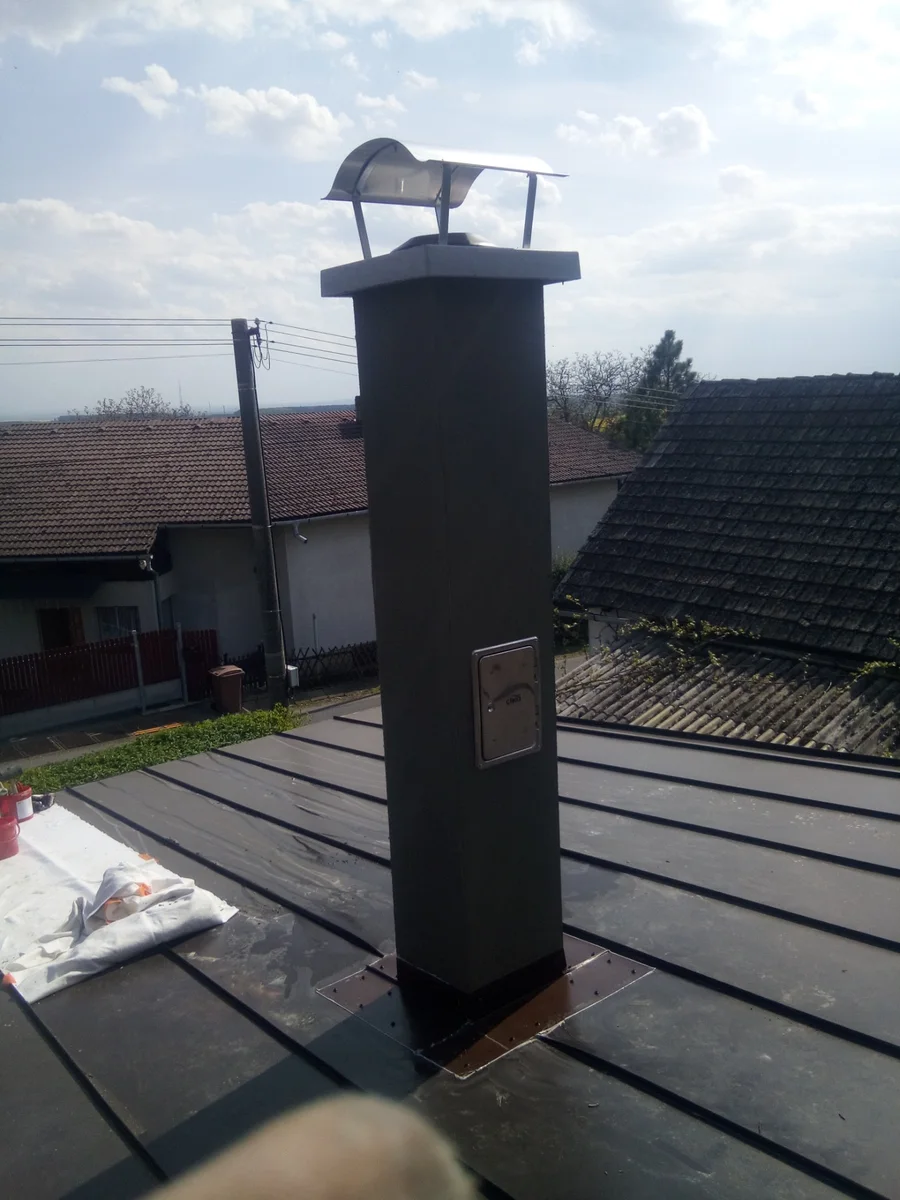 Černý komínový systém vyvedený nad falcovanou plechovou střechou rodinného domu